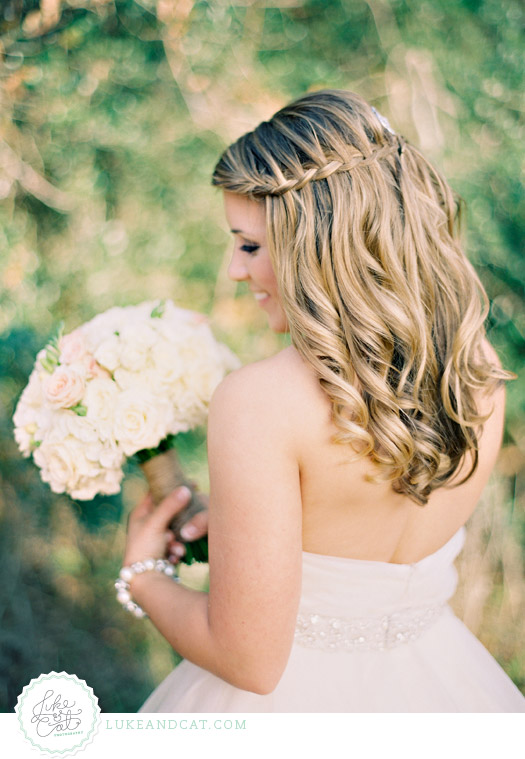 Elegant bride looking over shoulder with pink and white bouquet and waterfall braided hair.